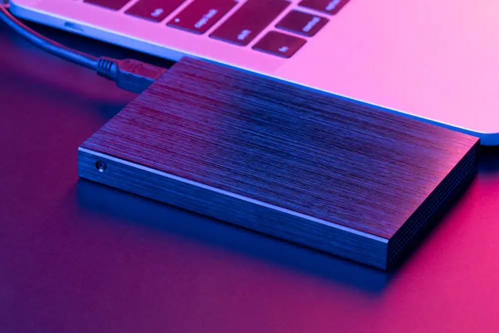 2TB external hard drive security - معرفی بهترین هارد اکسترنال 2 ترابایت در سال 1402 هارد اکسترنال مشکی در کنار لپ تاپ روی میز بنفش رنگ